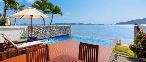 Una terraza de madera con piscina, sillones de descanso y vistas al mar.