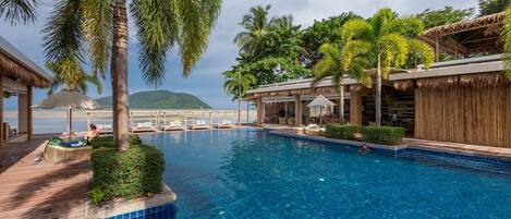 A swimming pool with lounge chairs and umbrellas, surrounded by palm trees and a wooden deck.