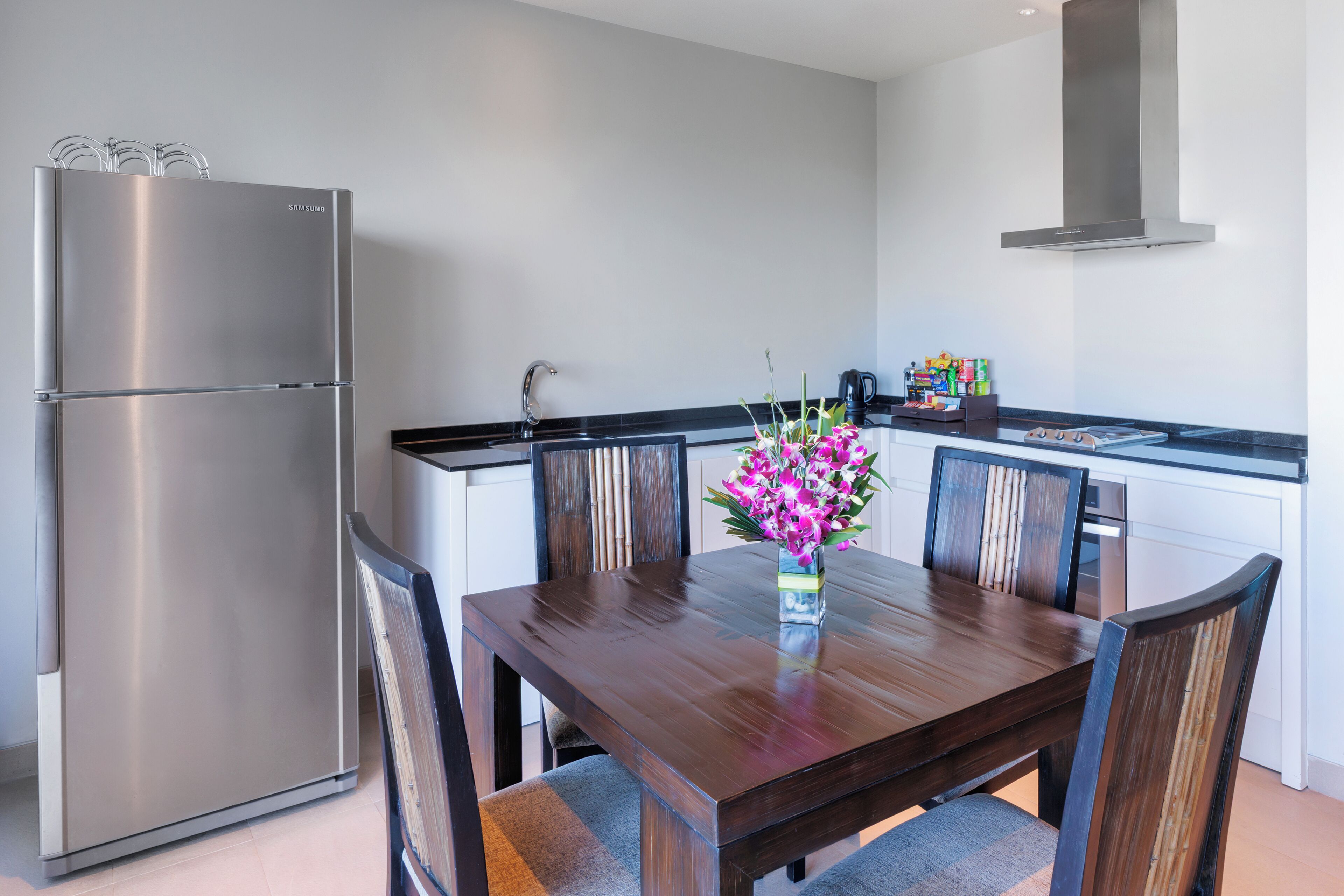 A modern kitchen with a stainless steel refrigerator, wooden dining table, and chairs.