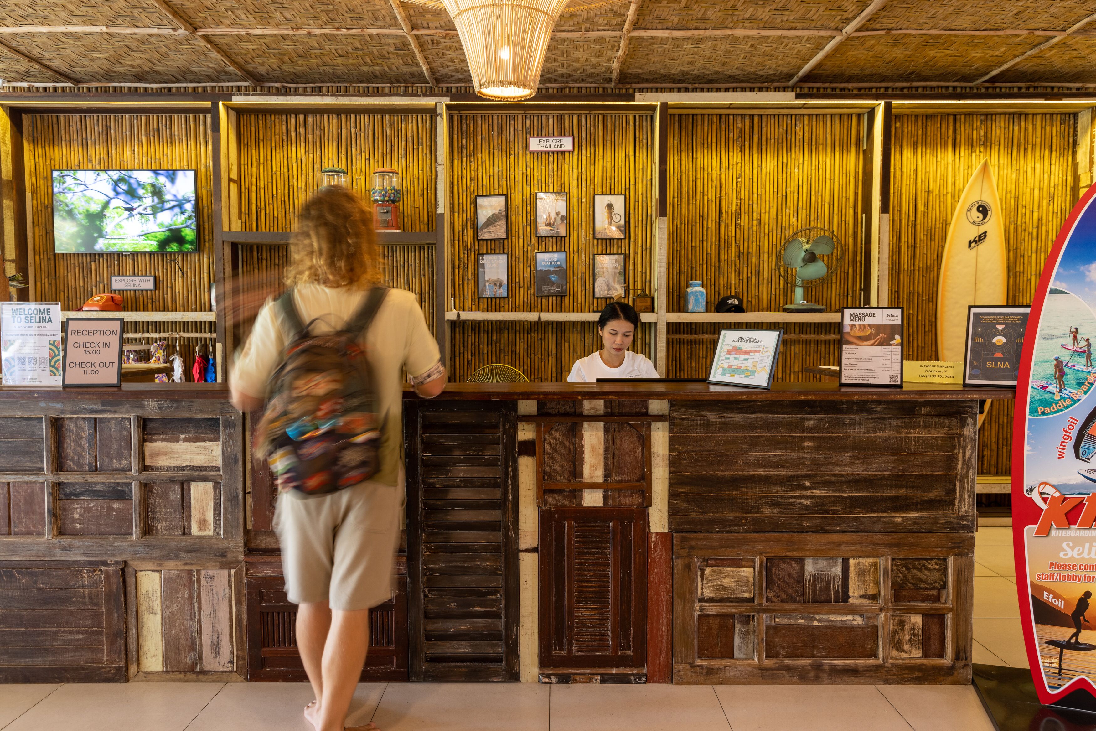 A reception area with a wooden reception desk, a television mounted on the wall, and a surfboard displayed on the wall.