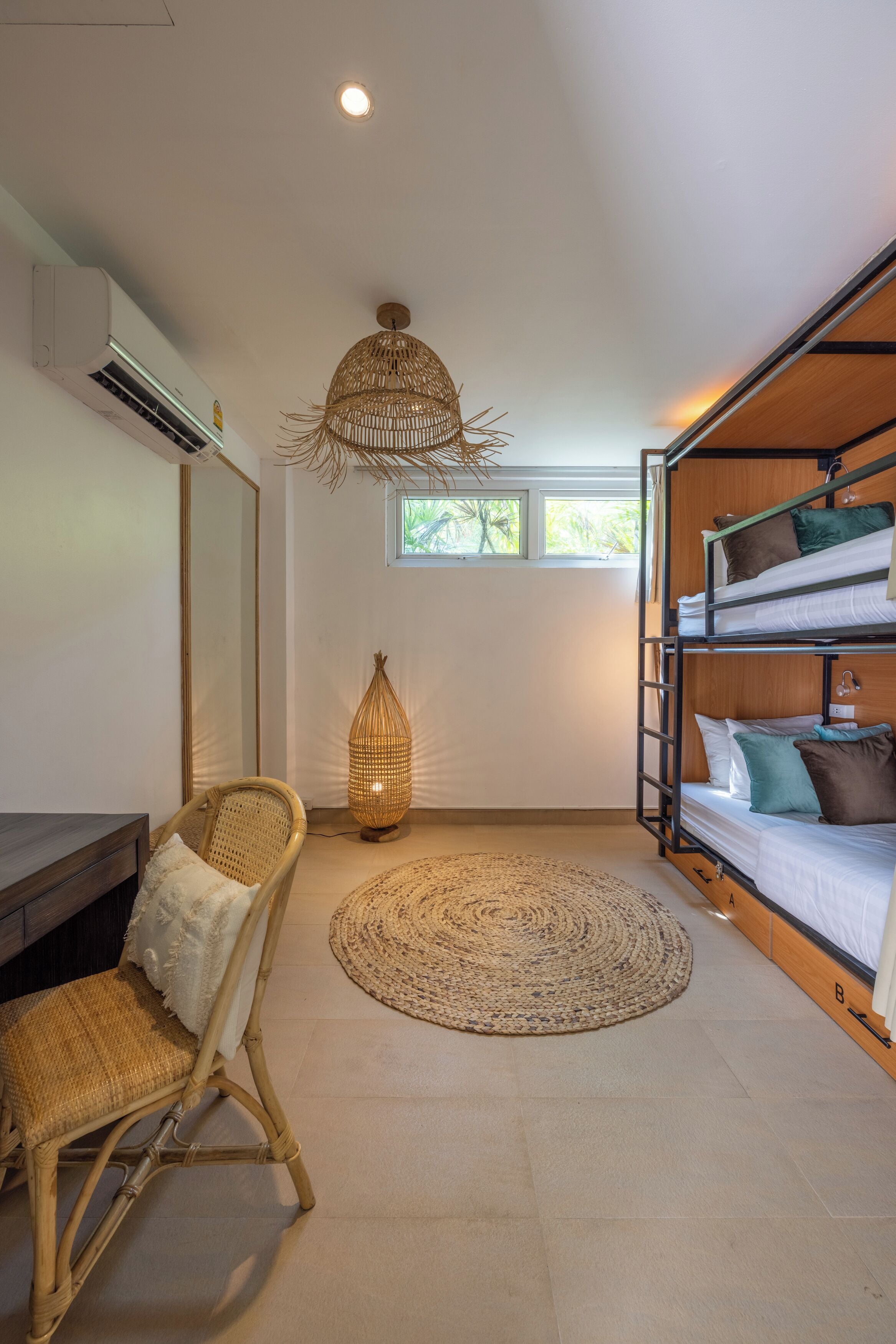 A compact room with bunk beds, a desk, a wicker chair, a woven floor rug, and a ceiling light fixture.