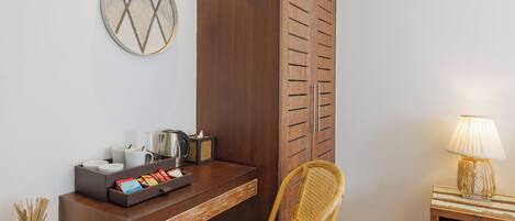 A room with a wooden desk, a wicker chair, a lamp, and a wardrobe.