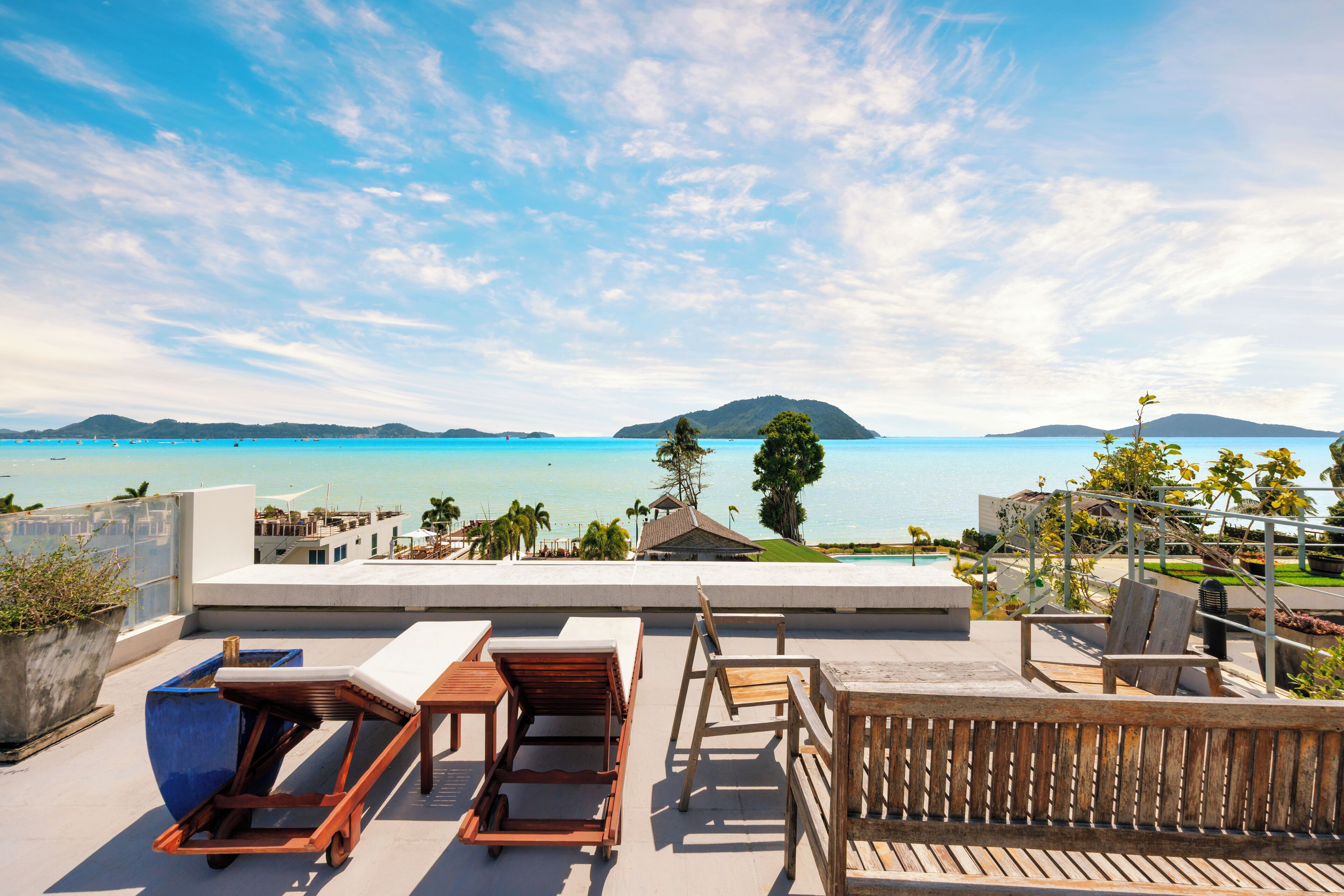 A rooftop terrace with lounge chairs, a table, and a view of the sea and distant islands.