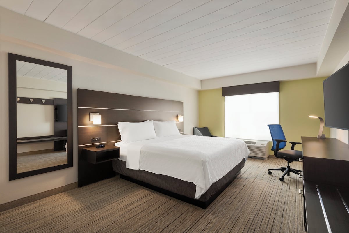 A modern hotel room with a large bed, a desk, a chair, and a mirror.