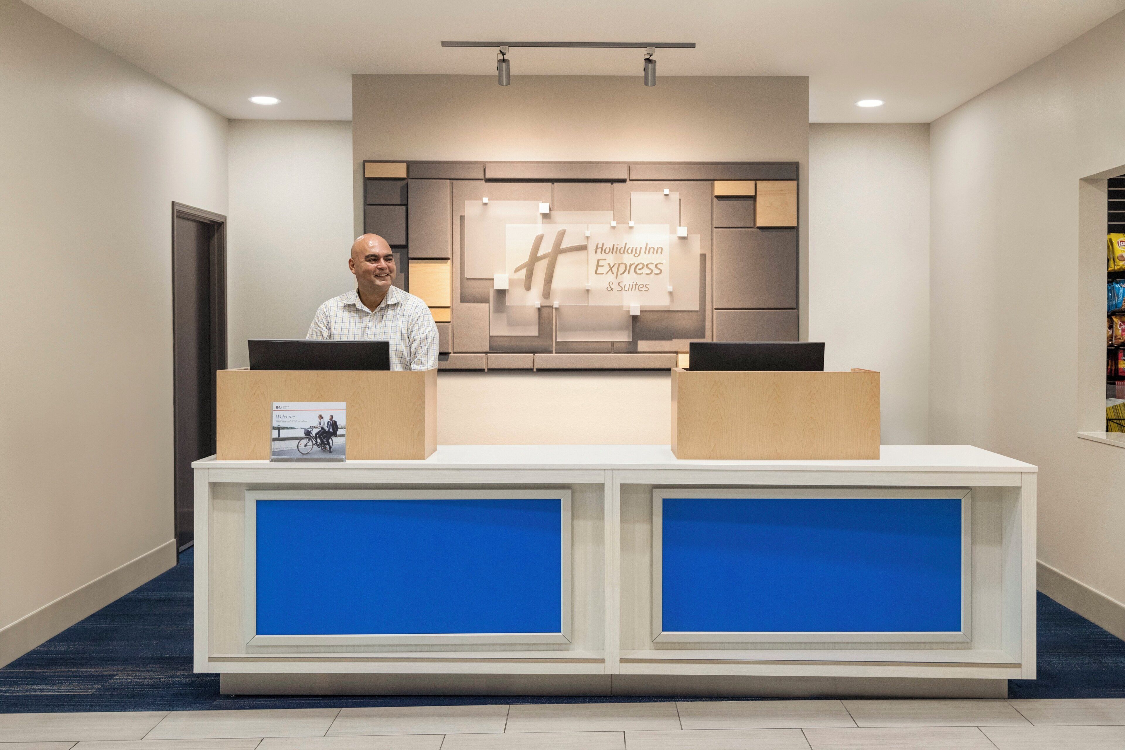 Un comptoir d’accueil avec une enseigne « Holiday Inn Express & Suites », deux postes informatiques et une brochure d’accueil.