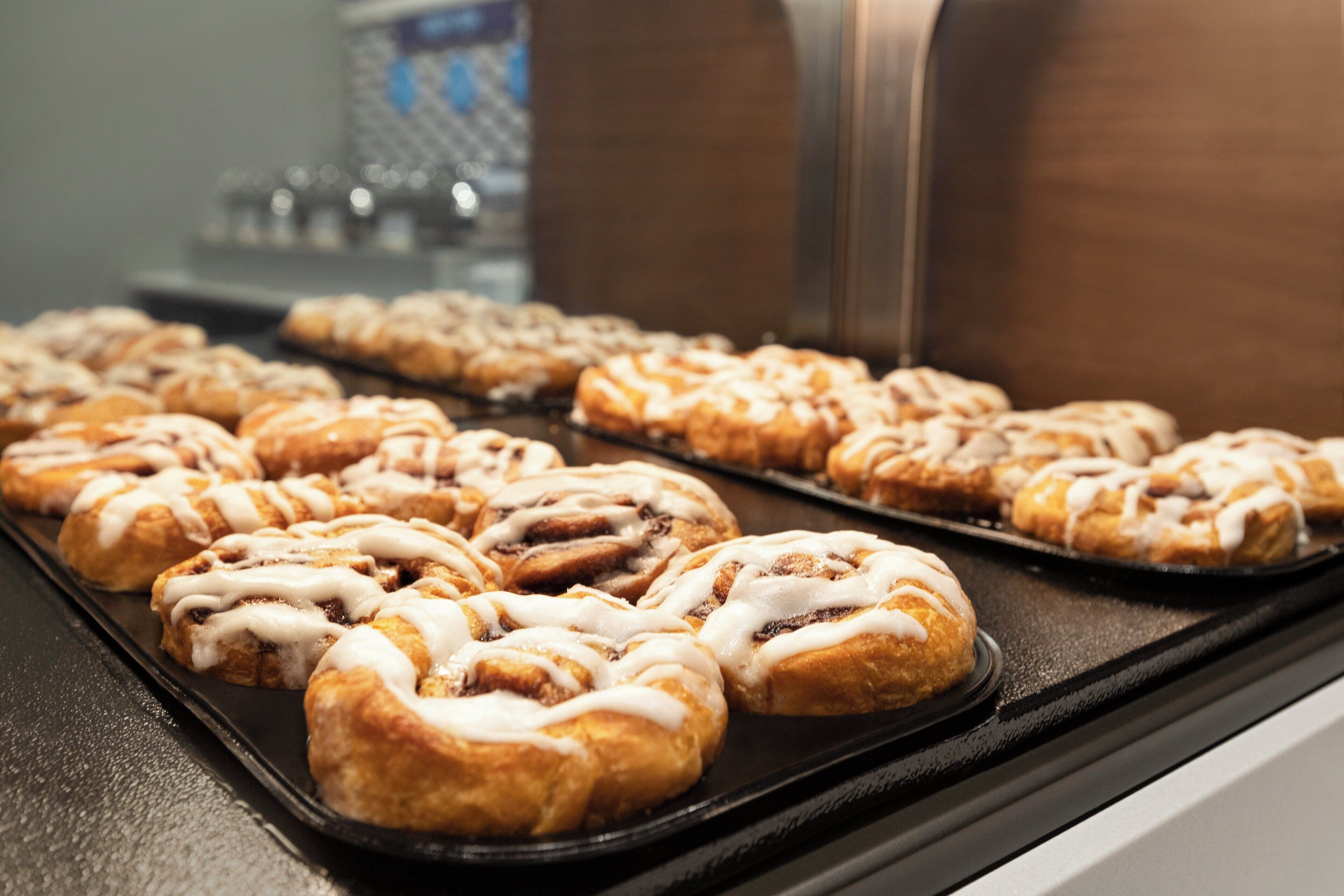 A tray of cinnamon rolls with icing on a black surface.