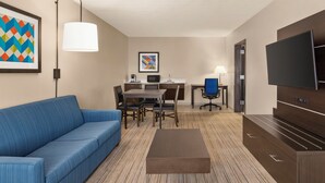 Une chambre d’hôtel avec un canapé bleu, une table à manger avec des chaises, un téléviseur et des œuvres d’art accrochées aux murs.