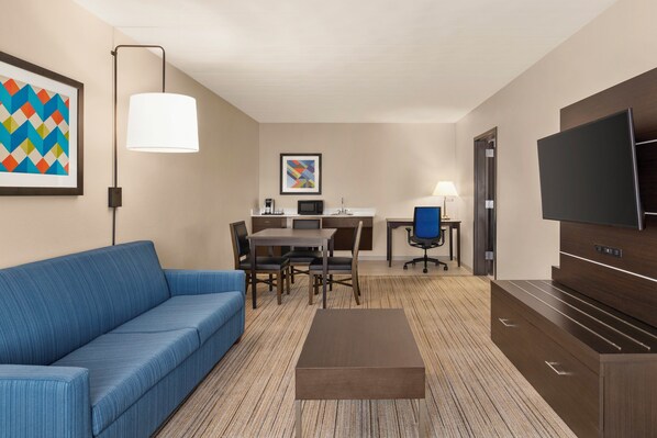 Een hotelkamer met een blauwe bank, een eettafel met stoelen, een televisie en kunstwerken aan de muren.