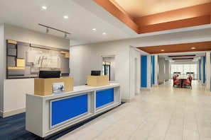 Een hotel receptie met een modern design, inclusief een receptiebalie, een digitaal display en een zithoek met tafels en stoelen.