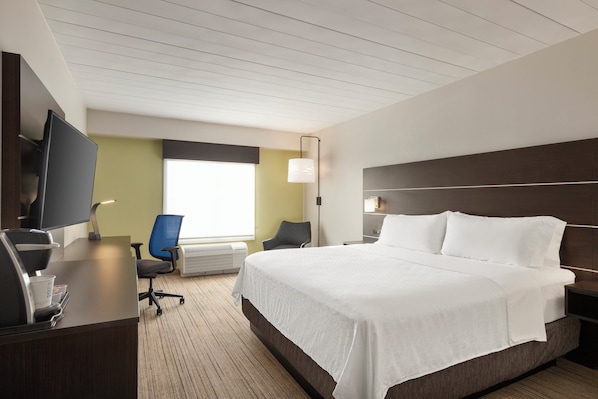 Habitación de hotel con una cama grande, un escritorio con computadora, una silla, un televisor y una ventana con persianas.