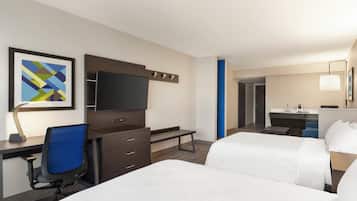 A hotel room with a bed, desk, chair, TV, and a bathroom visible in the background.