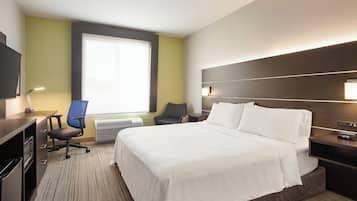 Quarto de hotel com uma cama grande, uma escrivaninha com computador, uma cadeira e uma televisão.