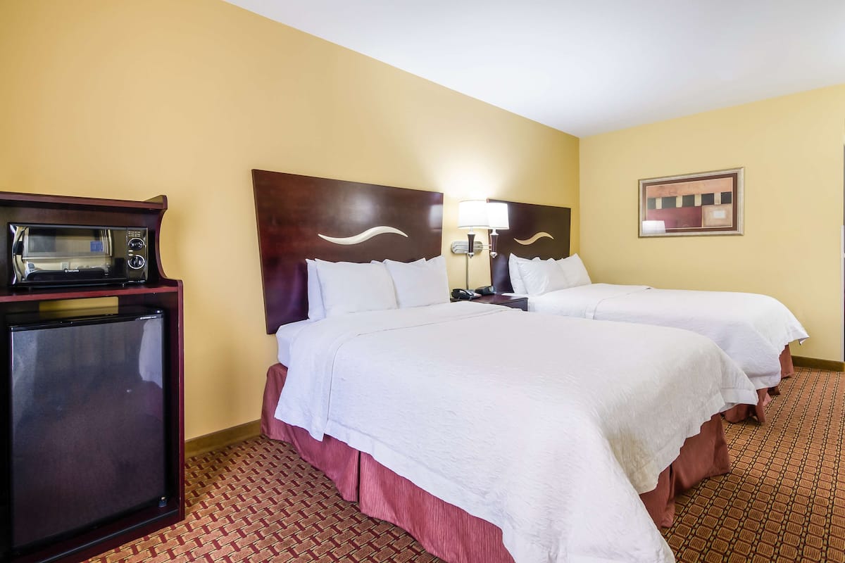 A hotel room with two beds, a microwave, a nightstand, and a lamp.