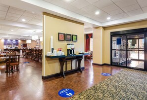 A hotel lobby with a reception desk, dining area, and a large glass door entrance.