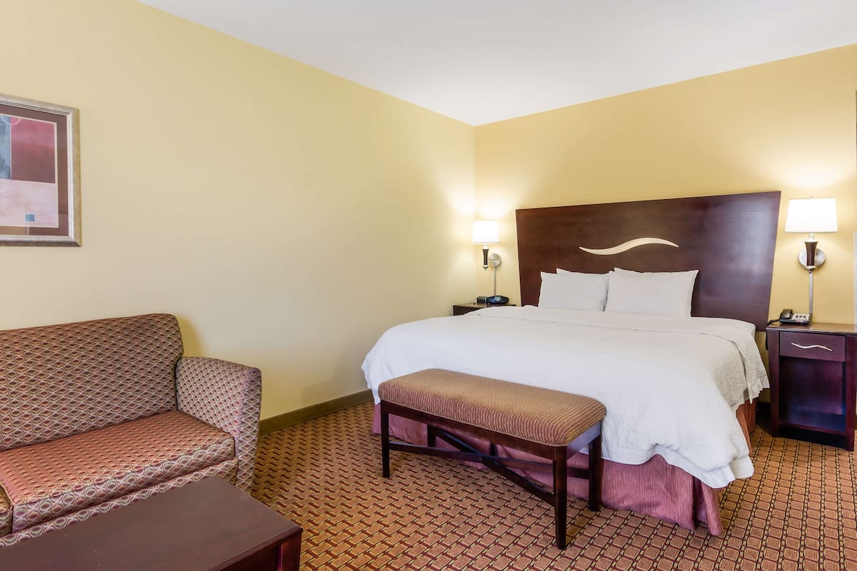 A hotel room with a bed, a bench, a sofa, and two bedside tables with lamps.