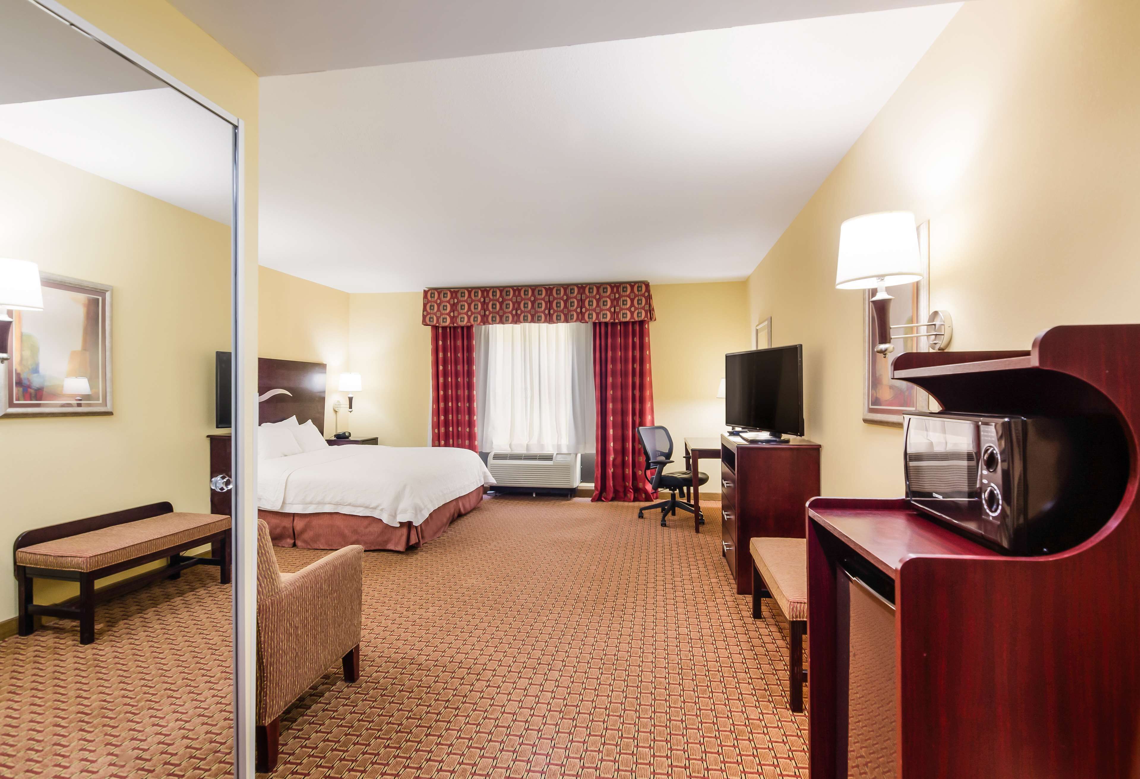 A hotel room with a bed, a desk, a chair, a television, and a microwave.