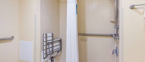 A shower area with a white curtain, grab bars, and a handheld showerhead.