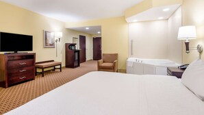 A hotel room with a bed, a desk, a chair, a television, a wardrobe, a bench, a bathroom with a bathtub, and a mirror. - Hampton Inn Galax (Galax)