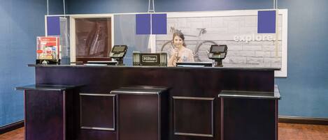 A reception desk with a 'Hilton Honors' sign, a bicycle in the background, and a 'Explore' sign on the wall.