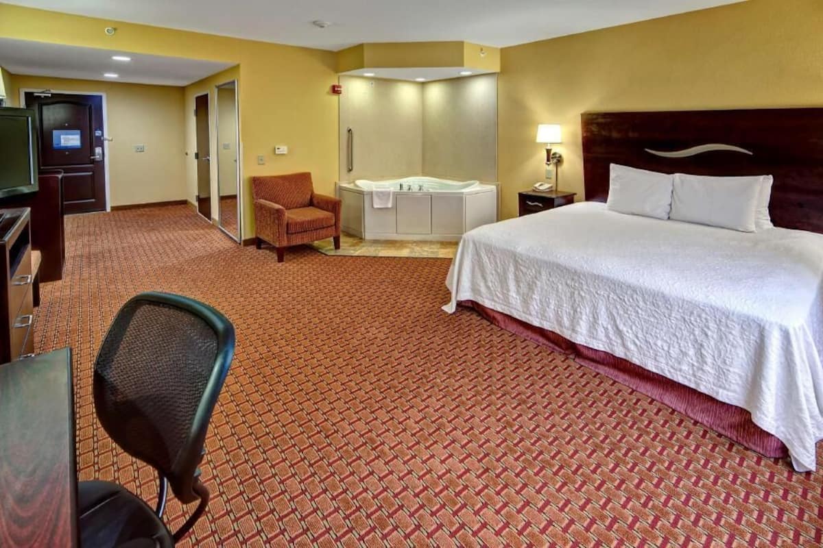 A hotel room with a bed, a desk, a chair, a television, a shower, and a bathroom.