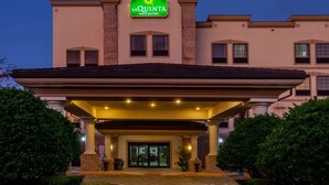 A hotel entrance with a covered area, columns, and a sign indicating it's a La Quinta Inn & Suites.