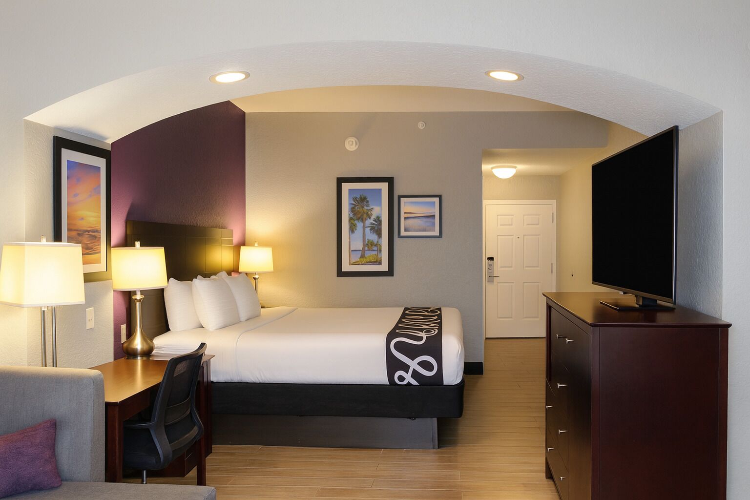 Een hotelkamer met een bed, bureau, stoel, televisie en een deur.