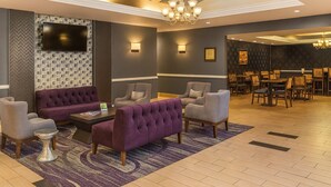 A lobby with a seating area featuring a sofa, armchairs, and a coffee table. There is a television mounted on a textured wall, and a chandelier hangs from the ceiling.