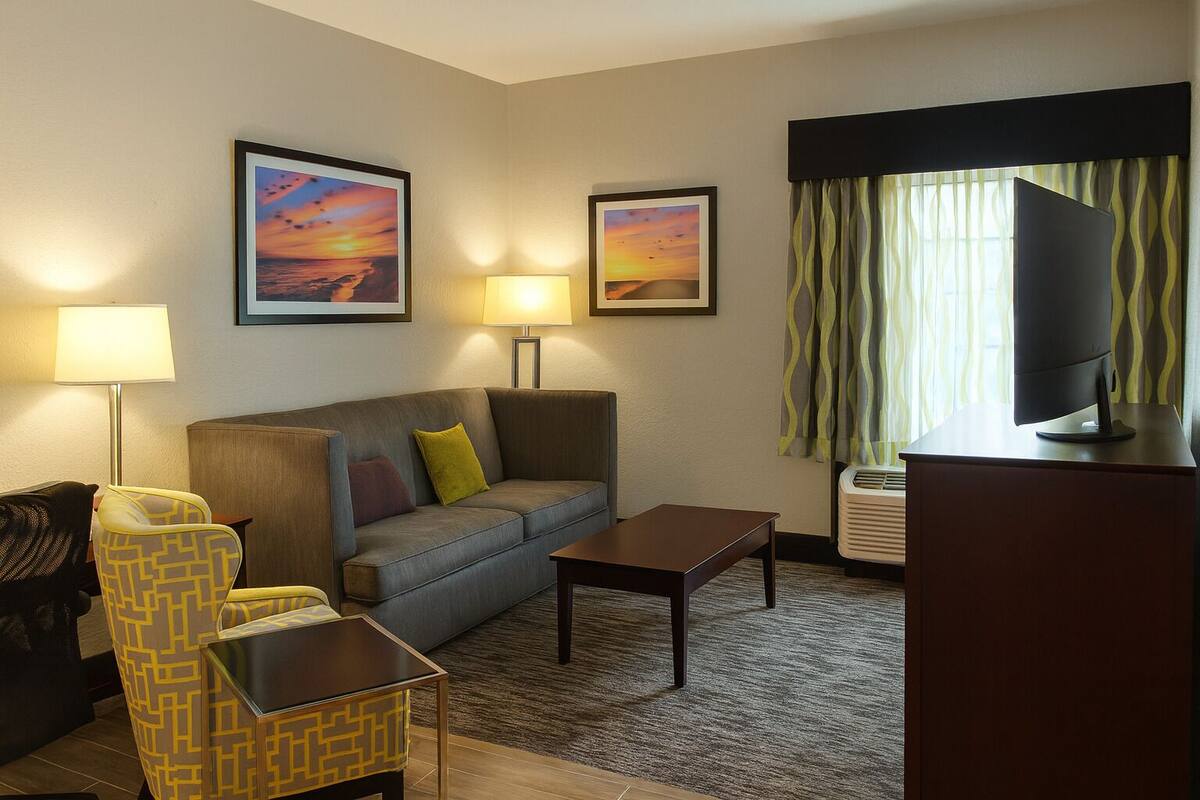A hotel room with a sofa, two armchairs, a coffee table, a TV, and two wall-mounted lamps.