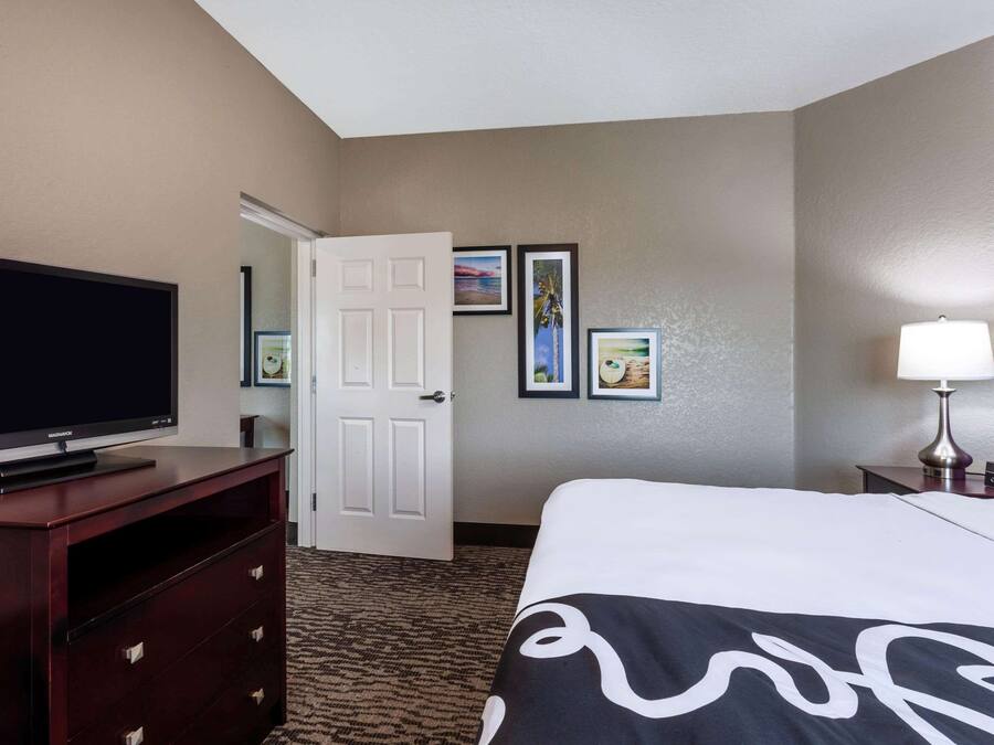 A hotel room with a bed, a television on a wooden dresser, a door, and framed pictures on the wall.