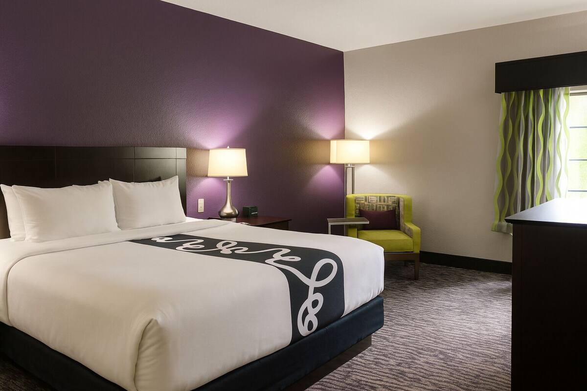 A hotel room with a large bed, two bedside lamps, a chair, and a desk.