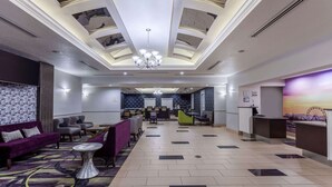 A hotel lobby with a high ceiling, a chandelier, seating areas, and a reception desk.