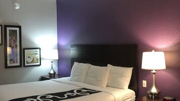 Ein Hotelzimmer mit einem großen Bett, einem Nachttisch mit Lampe und einem kleinen Tisch ebenfalls mit Lampe.