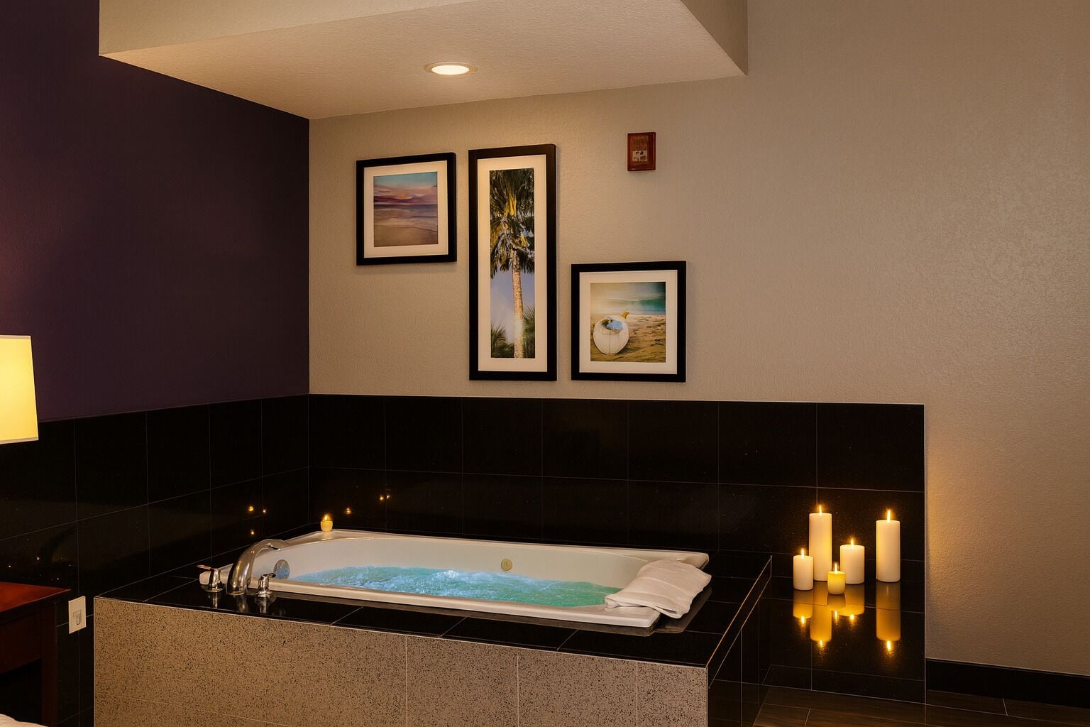 A modern bathroom with a large bathtub, black tiled walls, and framed pictures on the wall.