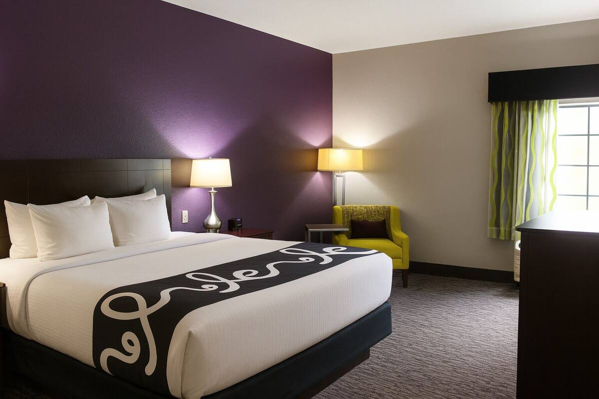 A hotel room with a large bed, two bedside lamps, a chair, and a window with curtains.