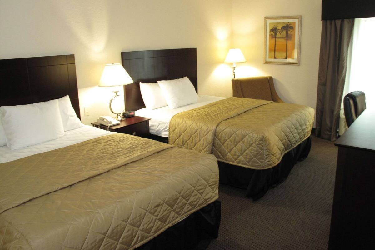 A hotel room with two beds, bedside lamps, a nightstand, and a painting on the wall.