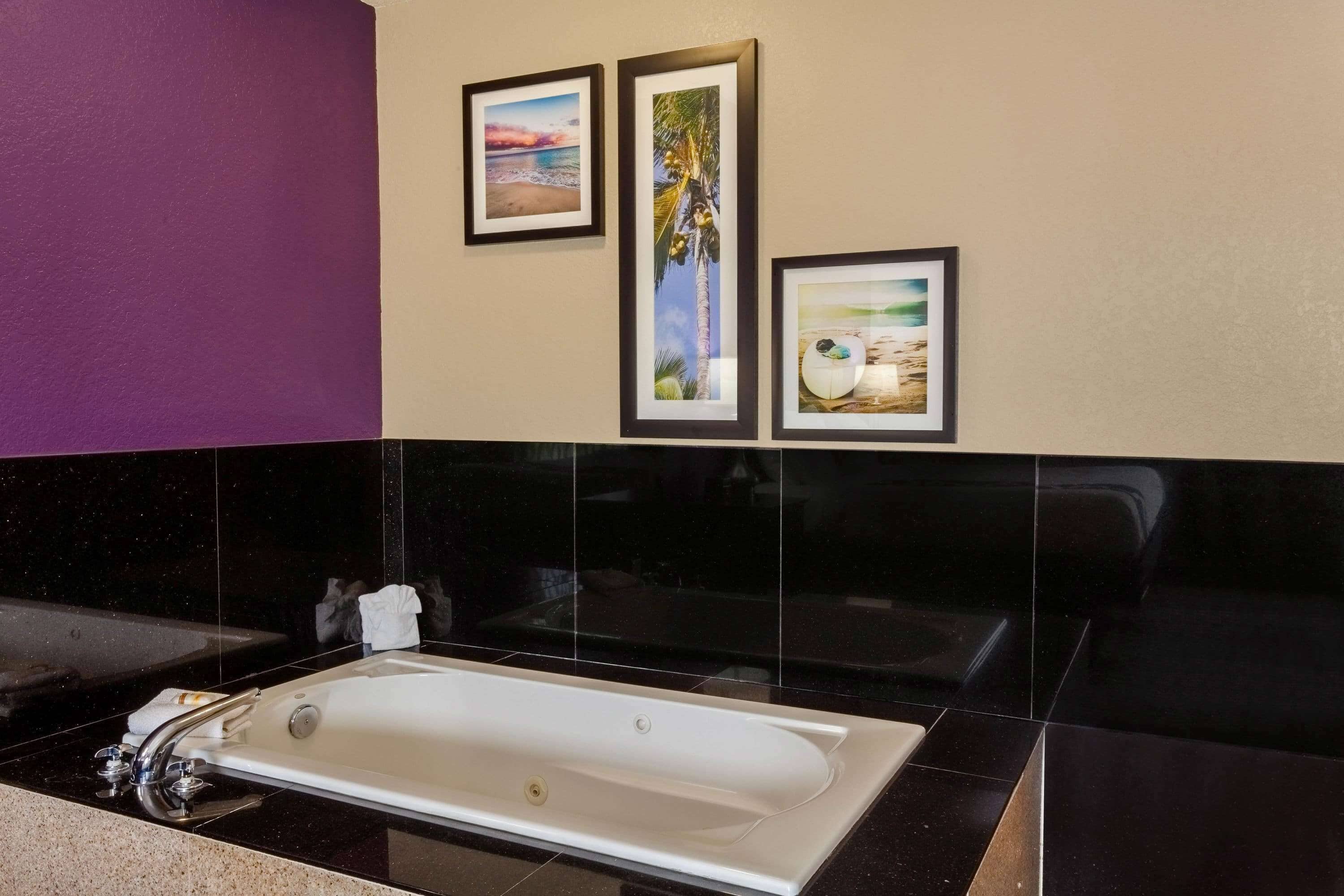 Un baño moderno con una bañera grande, paredes con azulejos negros y beige, y tres cuadros enmarcados.