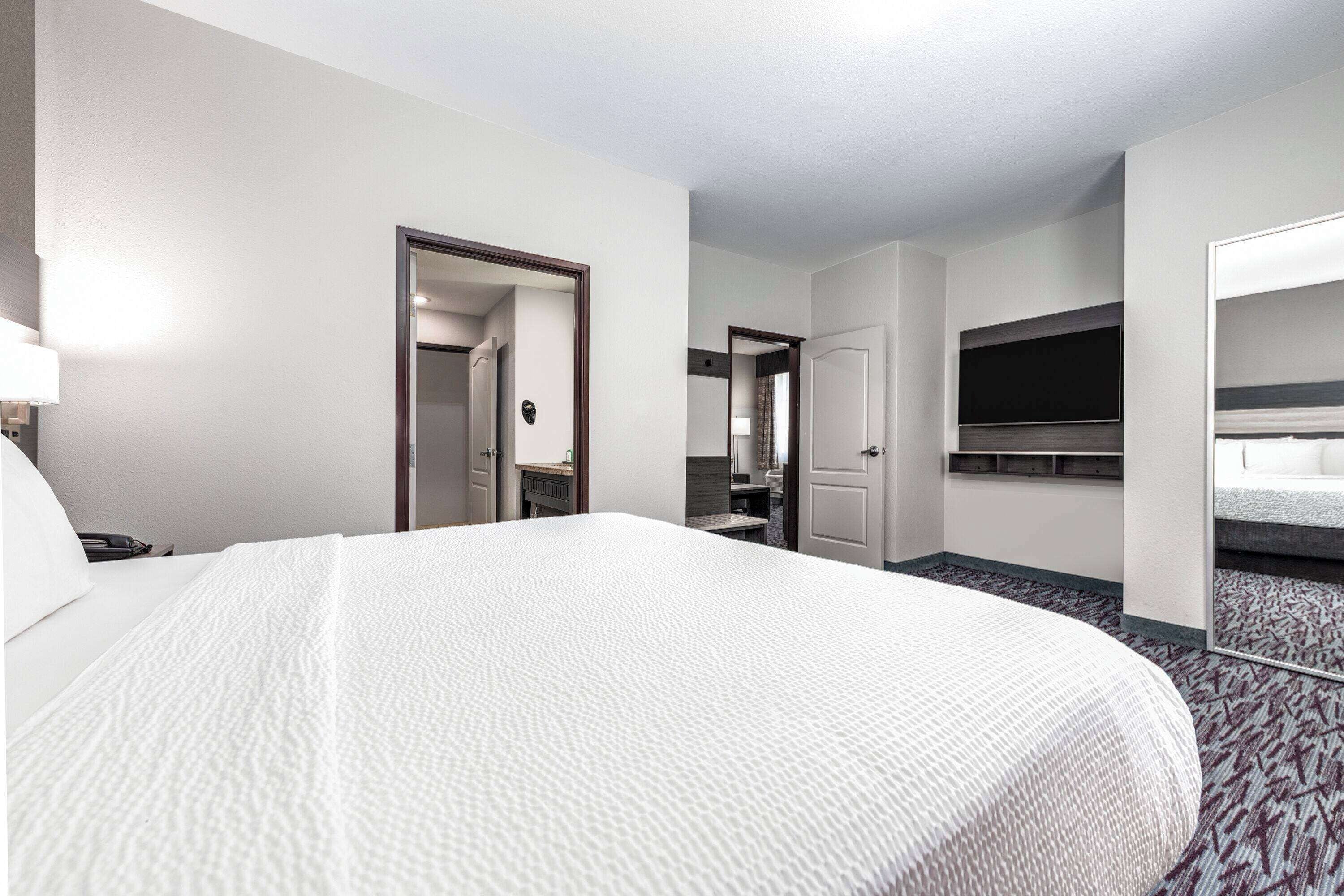 A hotel room with a large bed, a desk with a chair, a TV mounted on the wall, and a mirror.