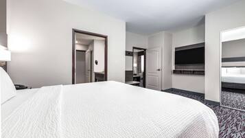 A hotel room with a large bed, a desk with a chair, a TV mounted on the wall, and a mirror.