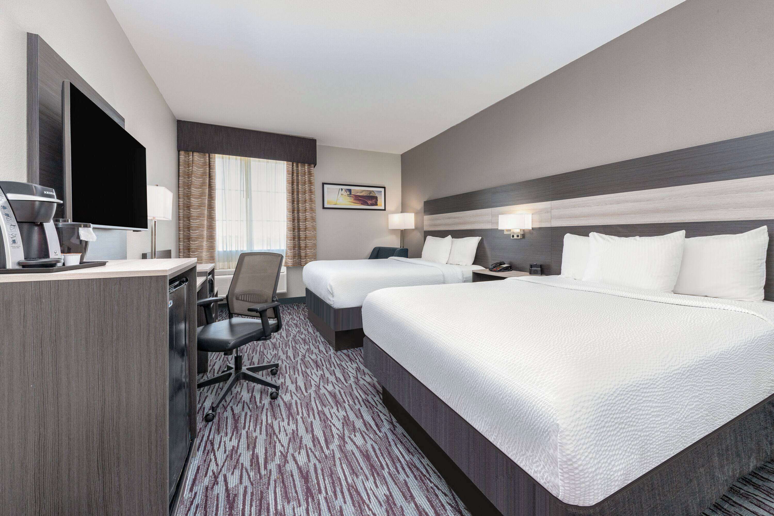 A hotel room with a large bed, a desk with a coffee maker, a TV, and a chair.