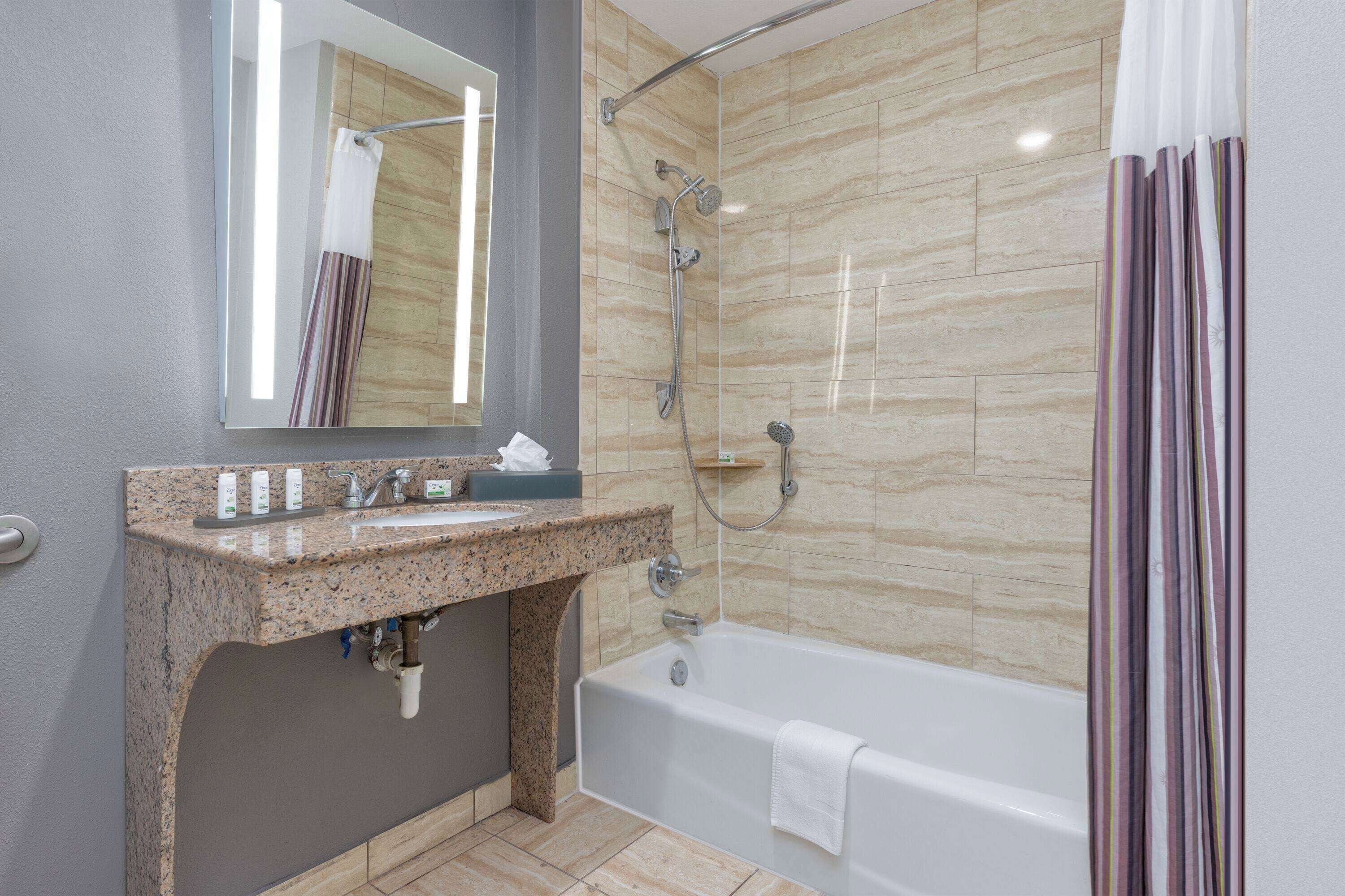 A modern bathroom with a granite sink, a mirror, a shower with a handheld showerhead, and a bathtub.