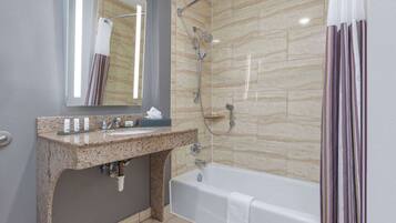 A modern bathroom with a granite sink, a mirror, a shower with a handheld showerhead, and a bathtub.