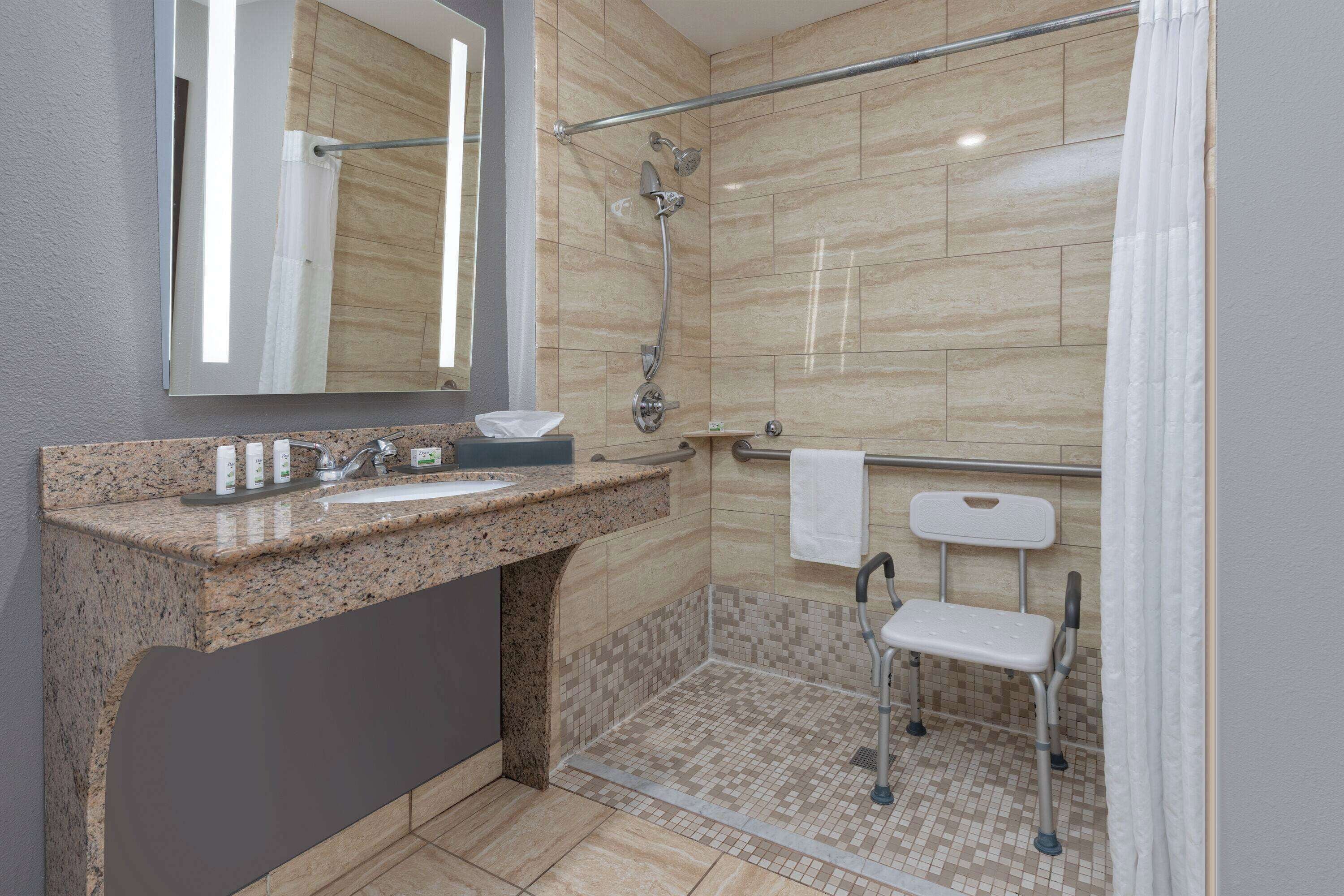 A modern bathroom with a granite countertop sink, a large mirror, a shower with a glass door, and a grab bar.