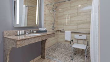 A modern bathroom with a granite countertop sink, a large mirror, a shower with a glass door, and a grab bar.