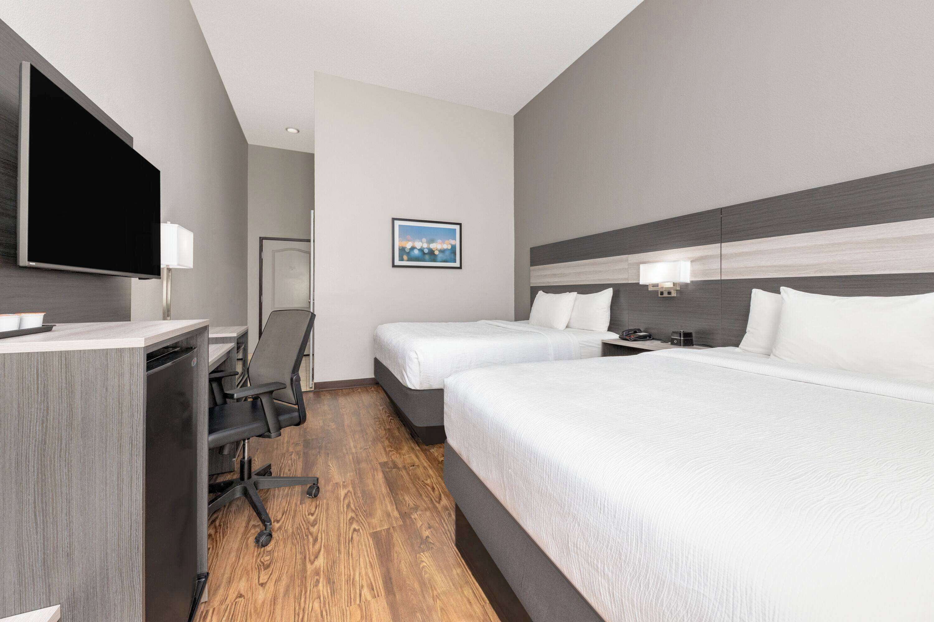 Een hotelkamer met twee bedden, een bureau, een stoel, een flatscreen televisie en een schilderij aan de muur.