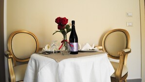Et spisebord med en vinflaske, en vase med en rød rose og to stole.