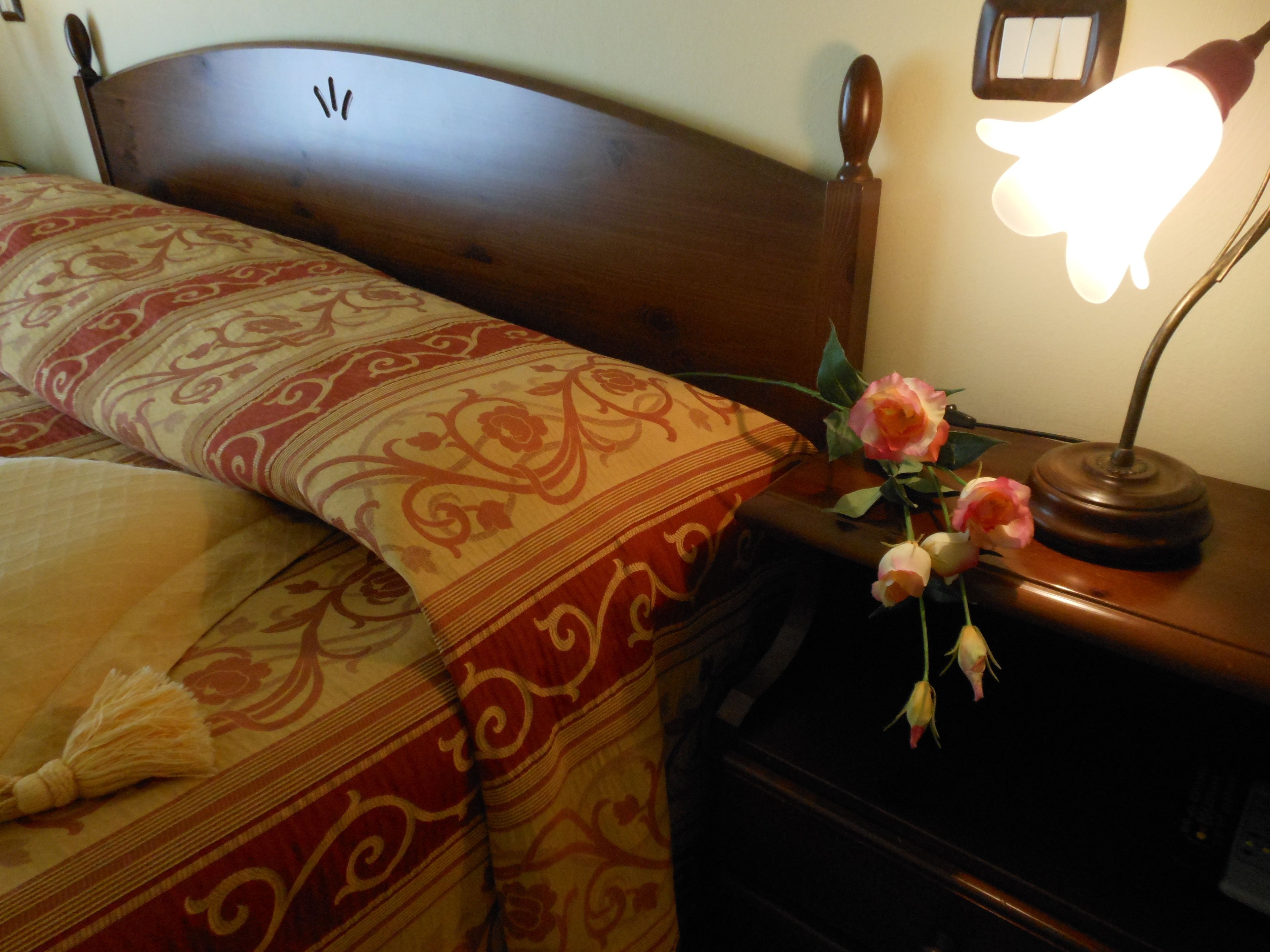 Un lit avec une couvre-lit à motifs, une lampe de chevet et un vase rempli de fleurs sur une table de chevet.