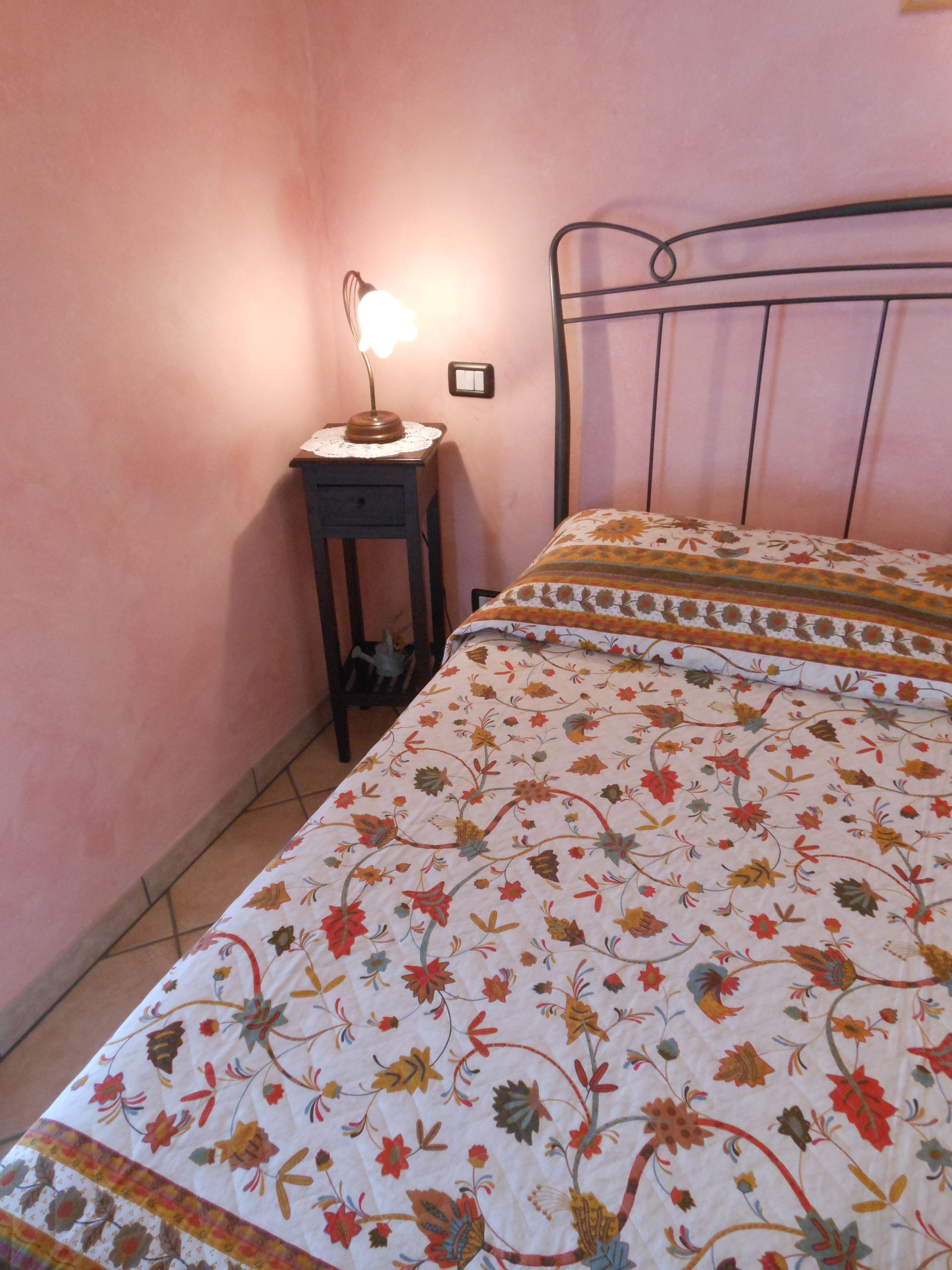 A bedroom with a floral bedspread, a bedside table with a lamp, and a metal bed frame.