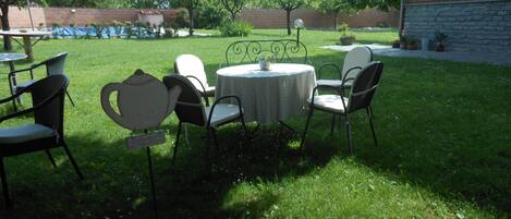 Un espacio de patio al aire libre con una mesa redonda y sillas, rodeado de césped y árboles.