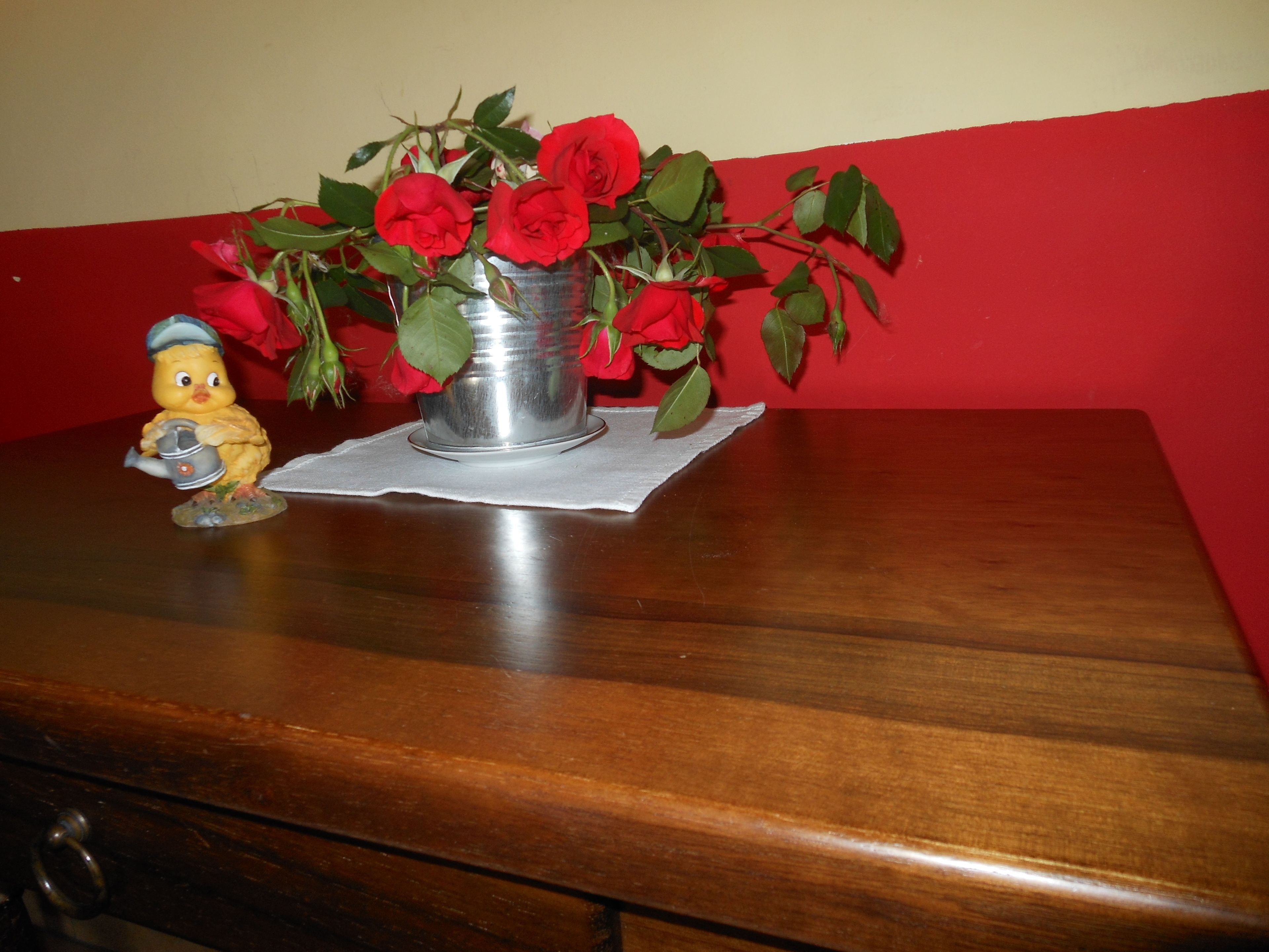 Une table en bois sur laquelle se trouve un vase en métal contenant des roses rouges et une figurine de canard en céramique.