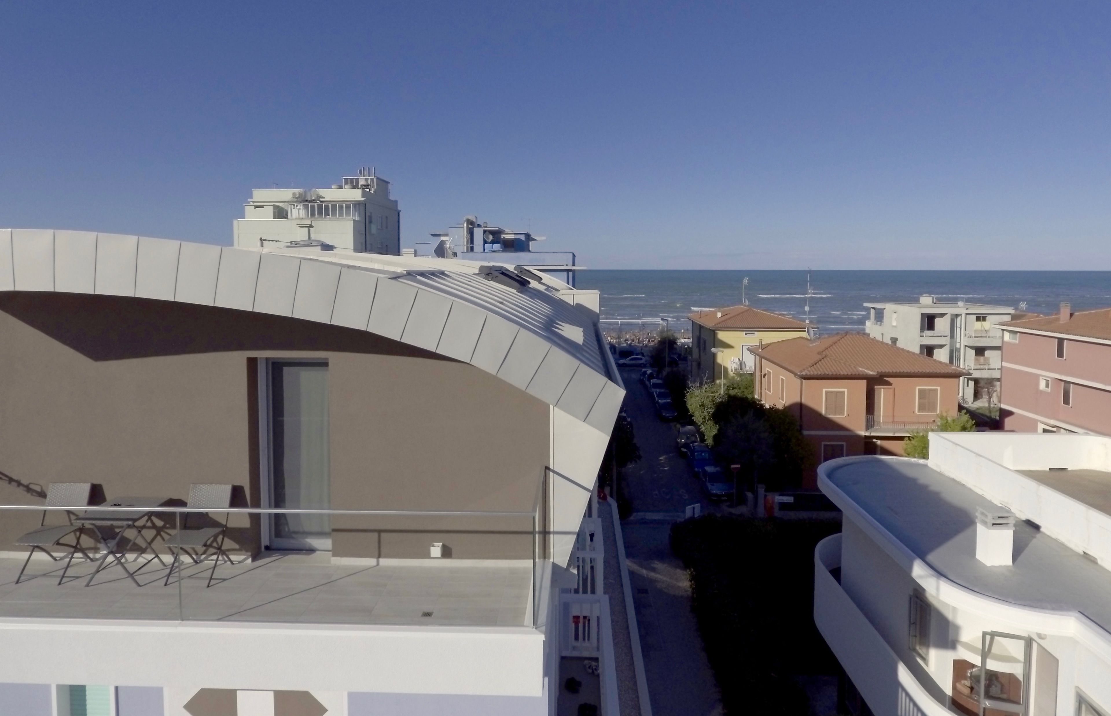 Un edificio moderno con un balcón curvo que da a una zona residencial y una vista despejada del mar.